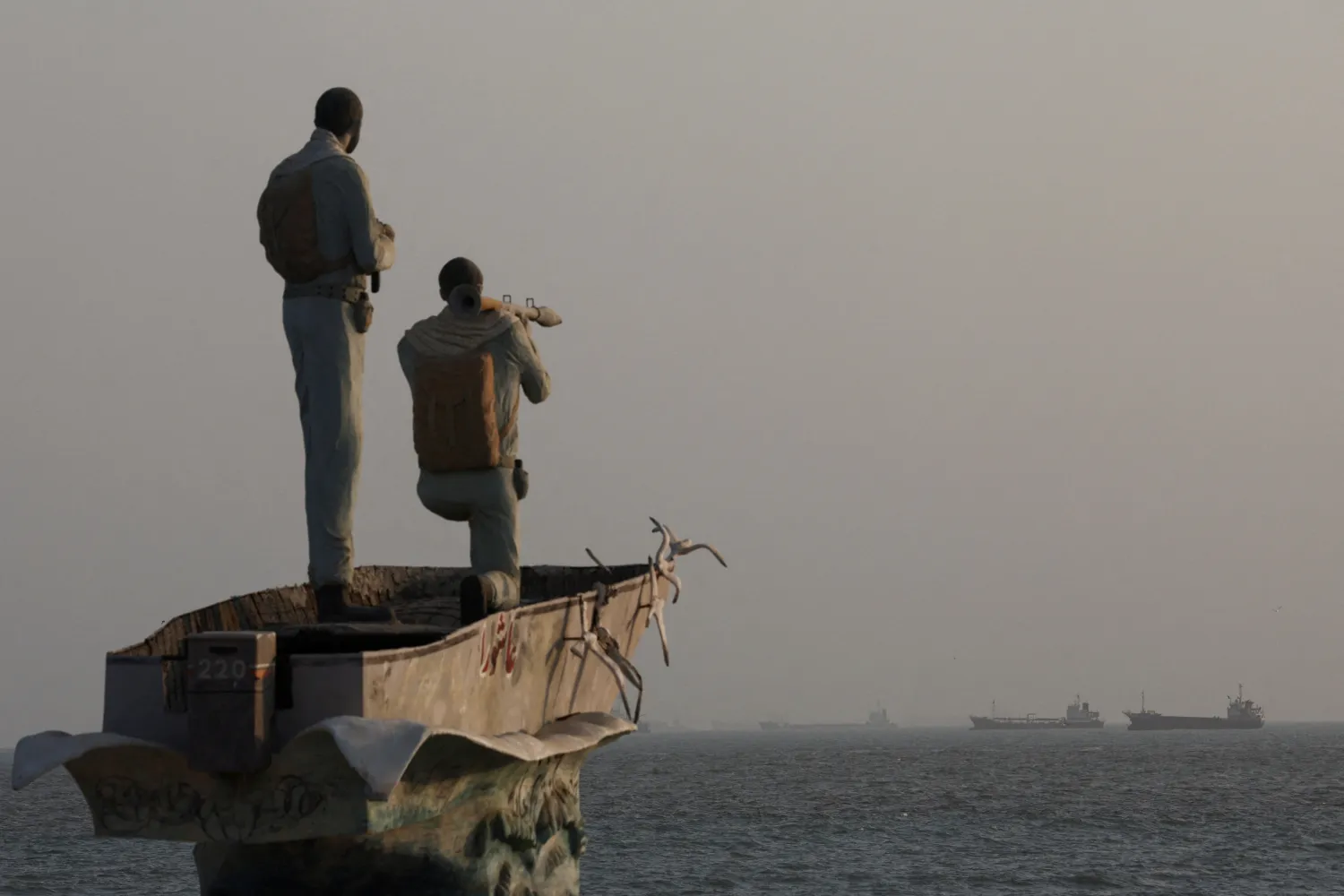 A statue of Iranian military members on the beach at Bandar Abbas, with ships visible in the Strait of Hormuz behind it